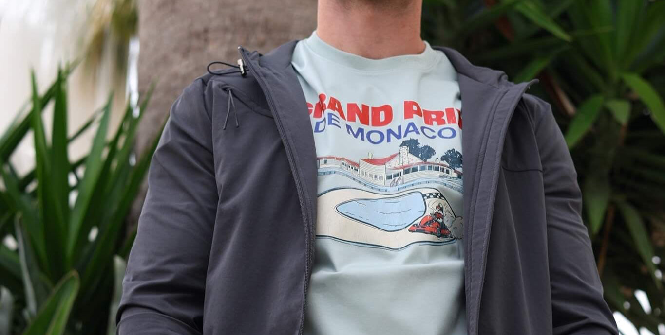 Man wearing a gray jacket over a graphic t-shirt with plants in the background
